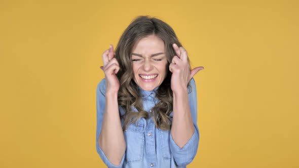 Worried Young Girl Standing with Finger Crossed for Good Luck on Yellow Background