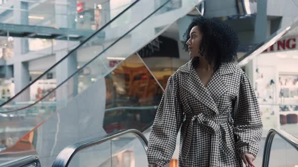 Stylish African American Woman with Colorful Shopping Bags in Their Hands Climbs the Escalator in