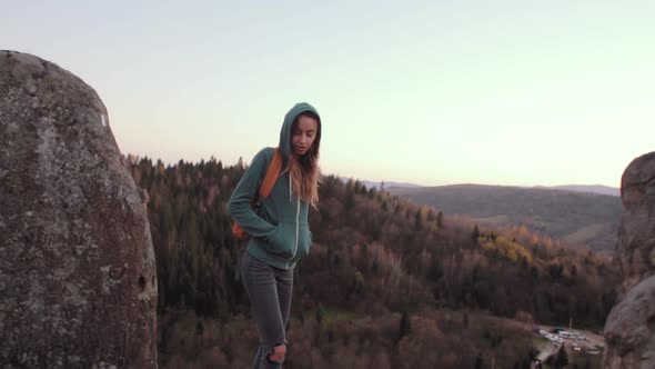 Woman Standing on Edge of Cliff Against a Forest Background