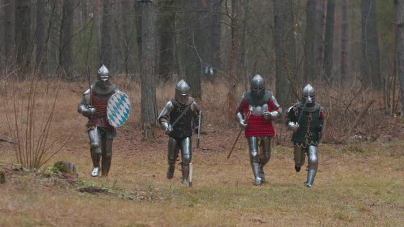 Four Men Knightes Running in the Row in the Forest in Full Armour Holding Weapons