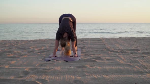 Female doing downward dog yoga on quiet beach at sunset