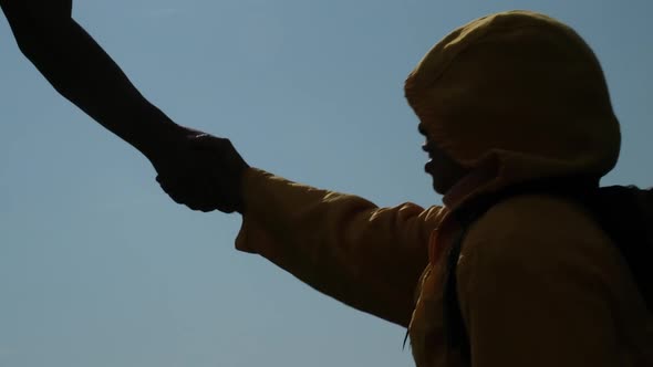 Silhouette of Asian couple climbing mountain, helping each other climb to the top of the mountain