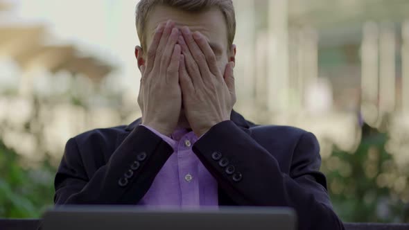 Tired Businessman Taking Off Glasses and Looking at Laptop