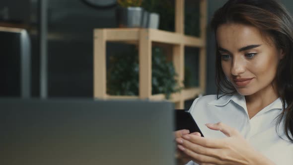 Freelancer Sitting in Cafe with Laptop and Using Phone with Smile at the Break