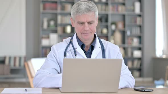 Professional Senior Doctor Working on Laptop While Sitting in Office