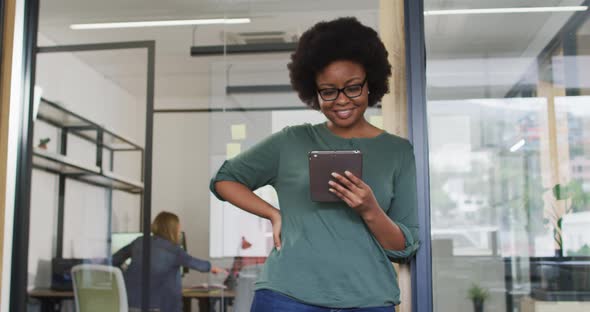 African american businesswoman leaning in doorway using tablet smiling to camera in office