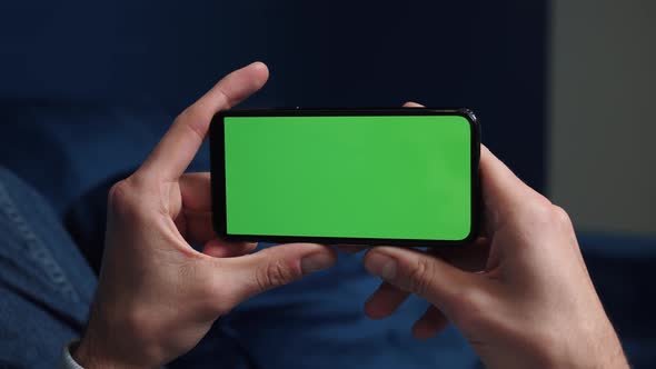 Close Up Shot of Guy Lying on Couch at Night, Holding a Smartphone with Chroma Key Mock Up Green