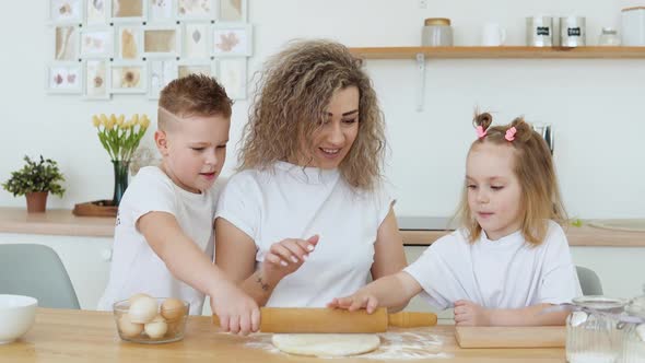 The Son and Daughter Help the Mother to Knead and Roll Out the Dough in the Kitchen in a