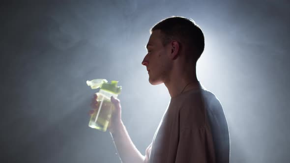 Young Man Opening Bottle and Drinking Water Standing in Dark Studio Background with White Light Side
