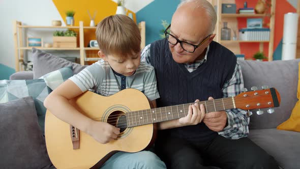 Old Man Teaching Talented Little Grandson To Play the Guitar in Apartment alt