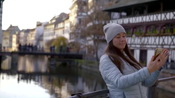 Portrait of a Cute Brunette with Long Hair and a Gray Hat on the Background of City Houses, River