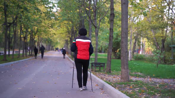 Full Length Rear View Portrait of Active Senior Woman Walking Towards Camera with Nordic Poles