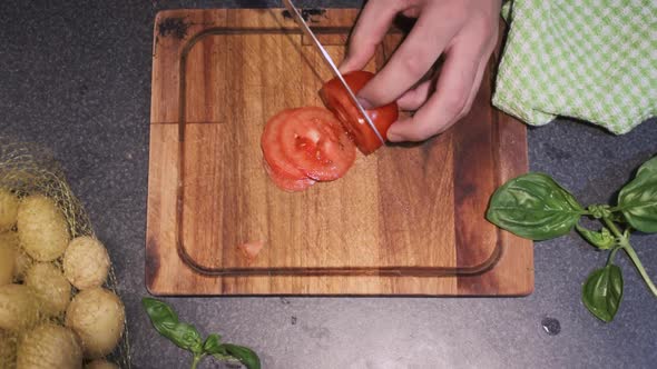 Young male slicing a tomato in his kitchen on top of a cutting board with a sharp knife