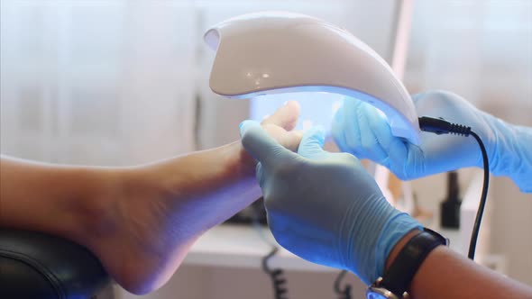 Pedicurist Master in Gloves is Drying Shellac on Toes with Special Uv Lamp