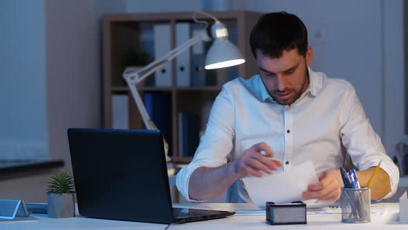 Businessman with Papers and Laptop at Night Office 24