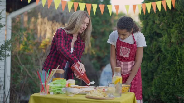 Concentrated Millennial Mother and Teenage Daughter Preparing Ingredients for Burgers on Picnic