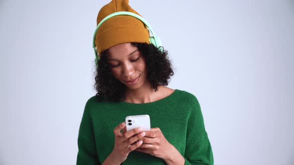 Happy curly-haired woman in headphones typing on the phone