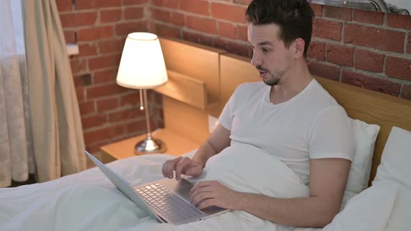 Young Man Celebrating Success on Laptop in Bed