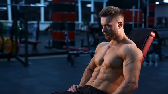 Strong handsome fitness trainer sits on sport chair and rests after training muscles.