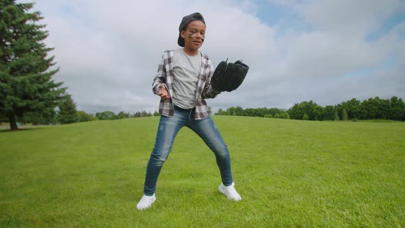 Joyful School Age African Boy with Baseball Glove and Ball Dancing on Field