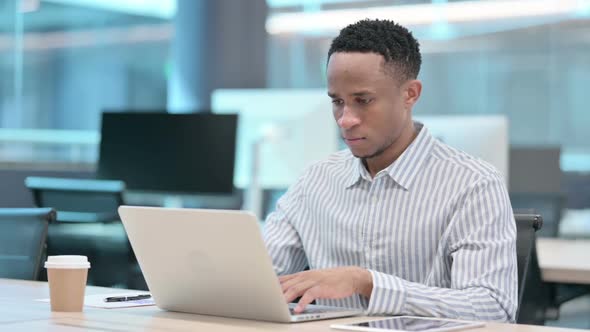 Attractive African Businessman Looking at Camera While Using Laptop in Office