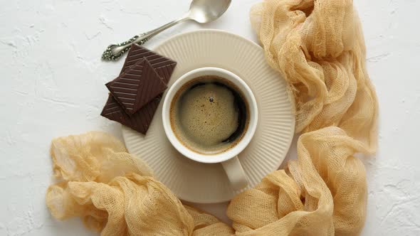 Black Coffee Cup with Dark Chocolate on Side. Placed on White Kitchen Table