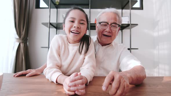 Senior Asian man and granddaughter talking via video call with family members.