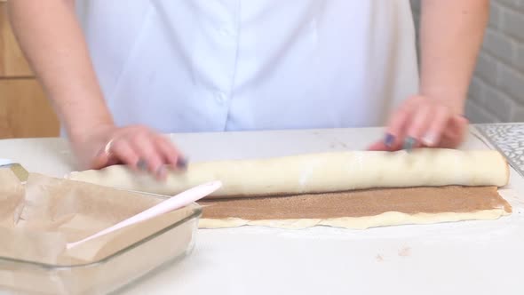 The Woman Rolls The Cinnabon Dough, Sprinkled With Cinnamon. On A White Tabletop. Close Up Shot