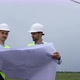 Men in white helmets hold project sheet, wind turbine generating electricity operation. - VideoHive Item for Sale