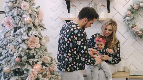 A Young Family in Warm Sweaters with a Baby Daughter in a Christmas Bedroom