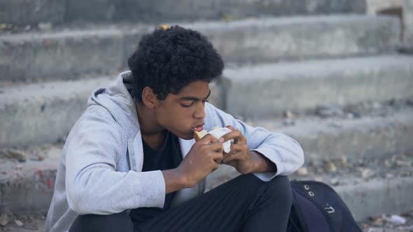 Hungry Afro-American Male Kid Eating Bread Looking Around, Street Lifestyle