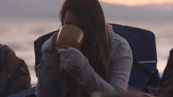 Young woman taking a sip from mug around campfire