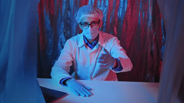 Doctor in eyeglasses, protective mask and gloves makes an inviting gesture in laboratory