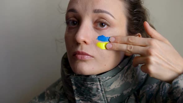 Young Girl is Paining Blue and Yellow Ukrainian Flag on Her Cheek Using Her Fingers Wearing Military