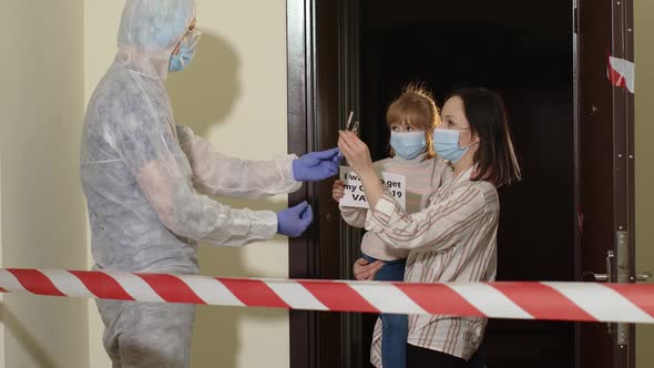 Doctor in Protective Suit with Vaccine Ampoule and Syringe Visiting Mother with Daughter at Home