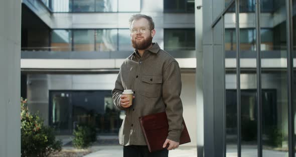 A Bearded Man Standing in the Courtyard of Office Center and Looking at Camera