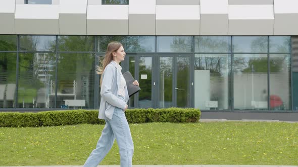 A Girl in a Business Suit with a Laptop in Her Hands Walks Down the Street