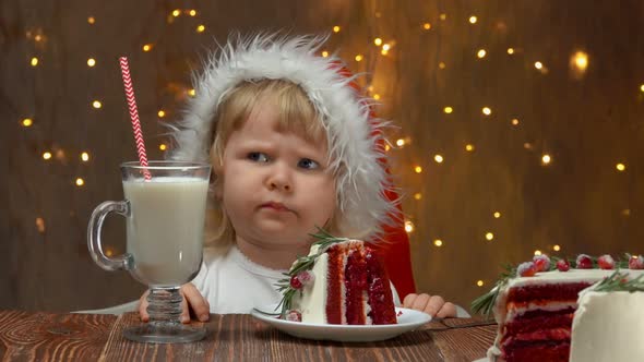 Sad Girl in Red Santa Claus Hat is Sitting Near the Table with Red Velvet Cake