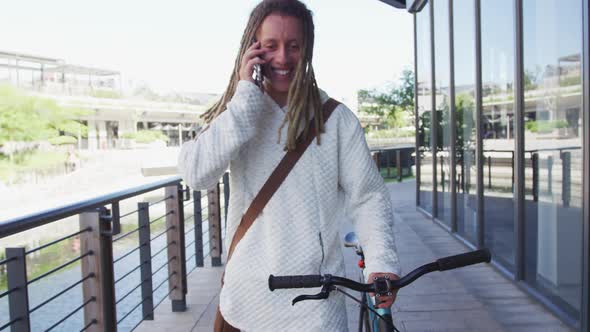 Mixed race man with dreadlocks wheeling a bicycle in the street talking on smartphone