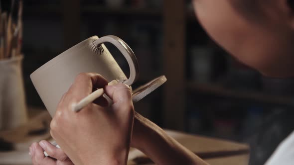 Young Woman Potter Putting on the Design to a Piece of Clay on the Edge of the Handle and the Cup