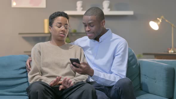 Couple Celebrating Success on Smartphone Sitting on Sofa