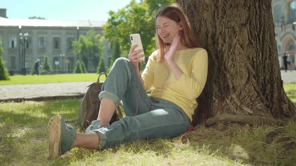 Cheerful Redhead Girl Using Video Chat Outdoors on Sunny Summer Day. Portrait of Positive Young