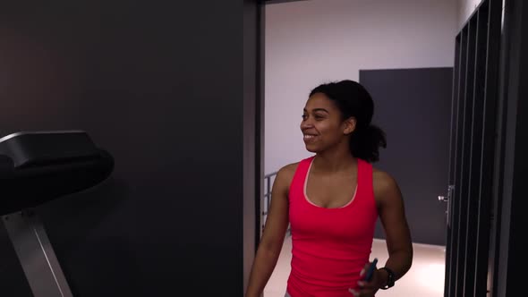 Black woman entering gym and greeting female friends running on treadmills