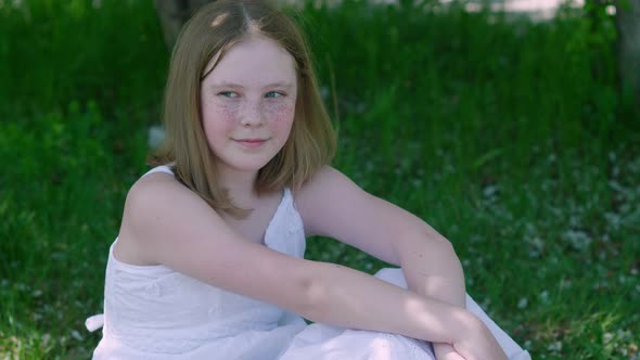 Beautiful Smiling Girl Sitting on Green Grass in Park