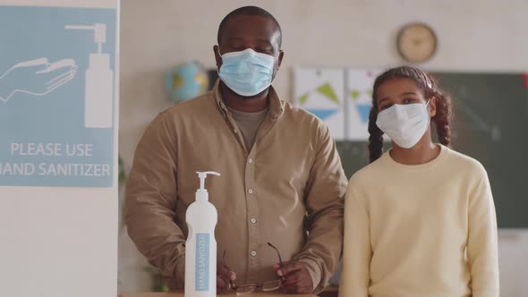 Portrait of Black Teacher and Schoolgirl in Face Masks Posing in Classroom