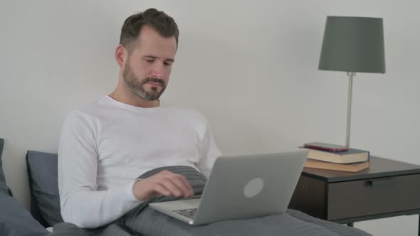 Man with Laptop Looking at the Camera in Bed
