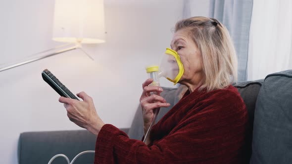 Elderly Woman Using Oxygen Mask While Changing Channels on Tv at Home