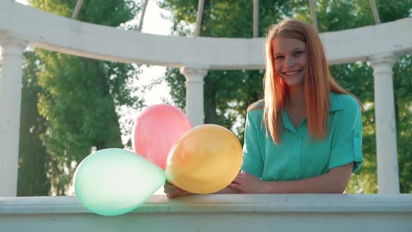 Beauty girl with red hair and colorful air balloons spinning and laughing, on white background. Beau