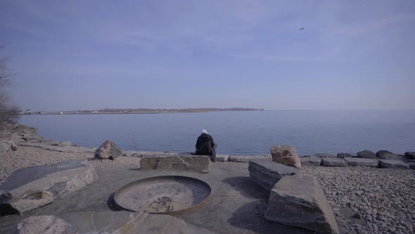 Person in Toronto Trillium Park with hijab sitting near lake in bright yellow jacket during day. Pro