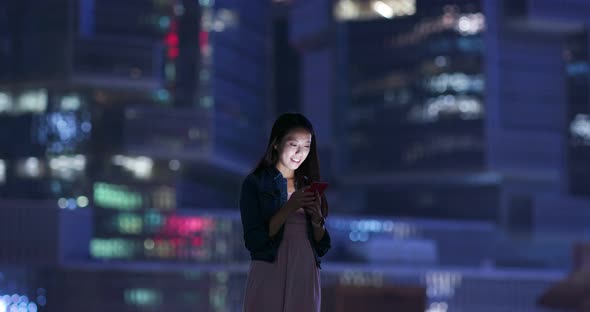 Woman look at mobile phone over business tower background at night